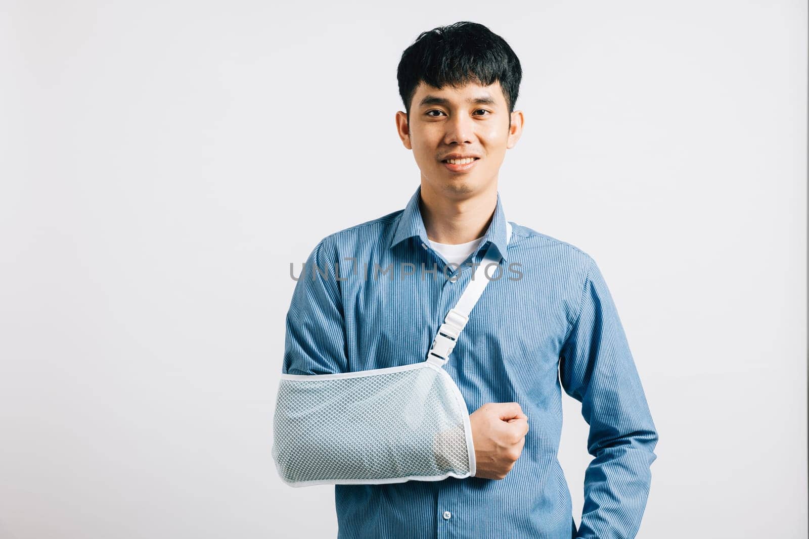 An optimistic businessman, despite his broken arm, smiles while wearing treatment splint. excited Asian man with arm support, studio shot isolated on white background, showcasing recovery. Copy space