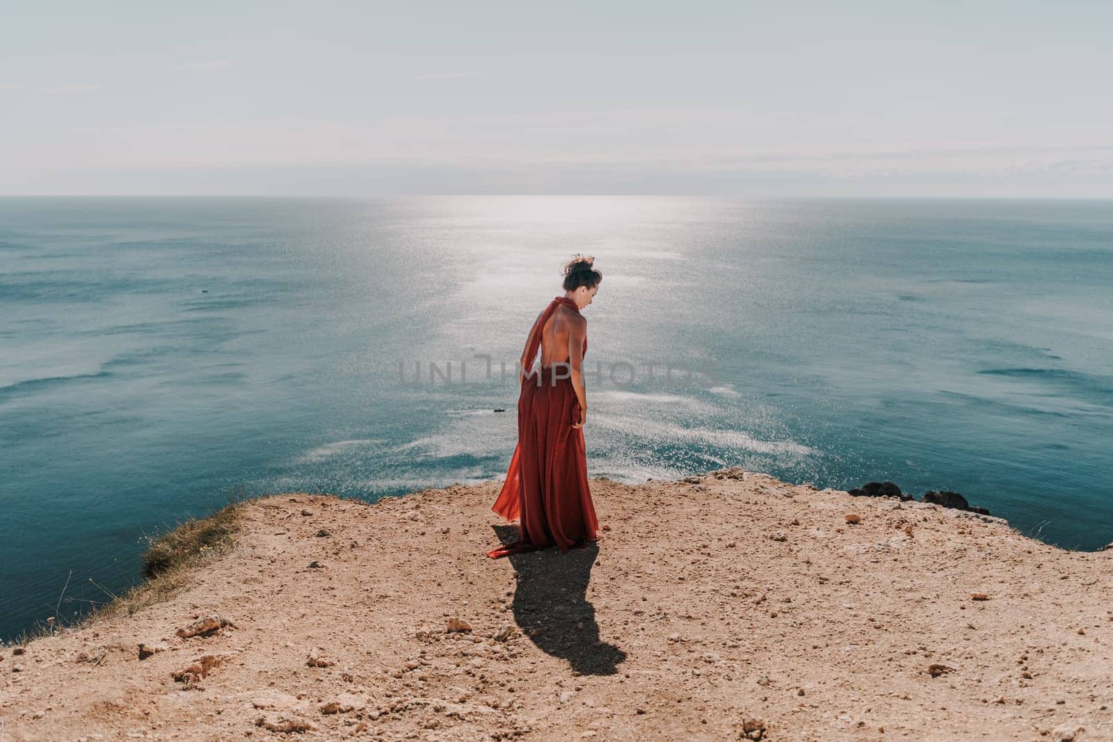 Woman red dress sea. posing on a rocky outcrop high above the sea. Girl on the nature on blue sky background. Fashion photo