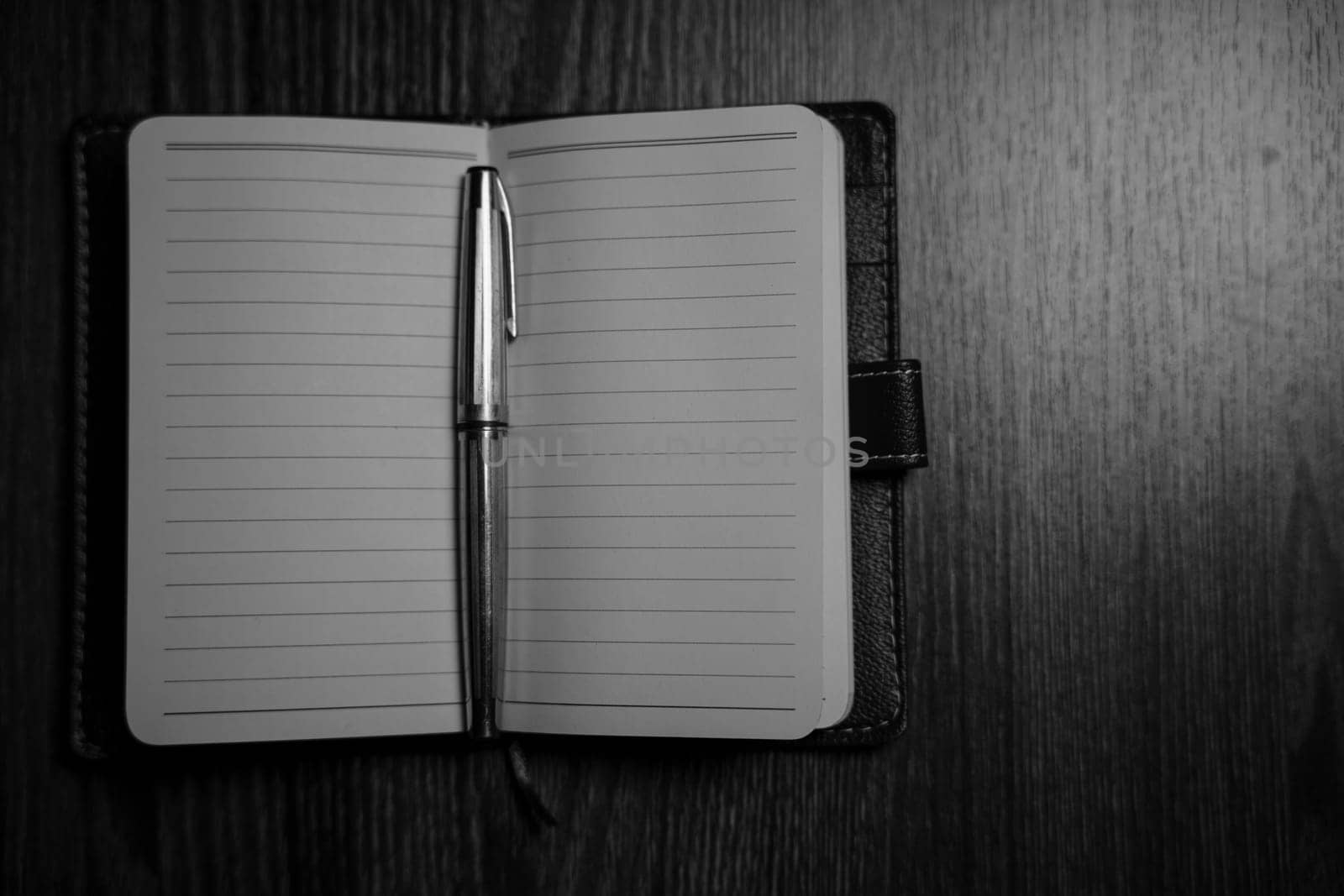 Black and white photo of the notebook with a pen on the table in the candlelight. High quality photo