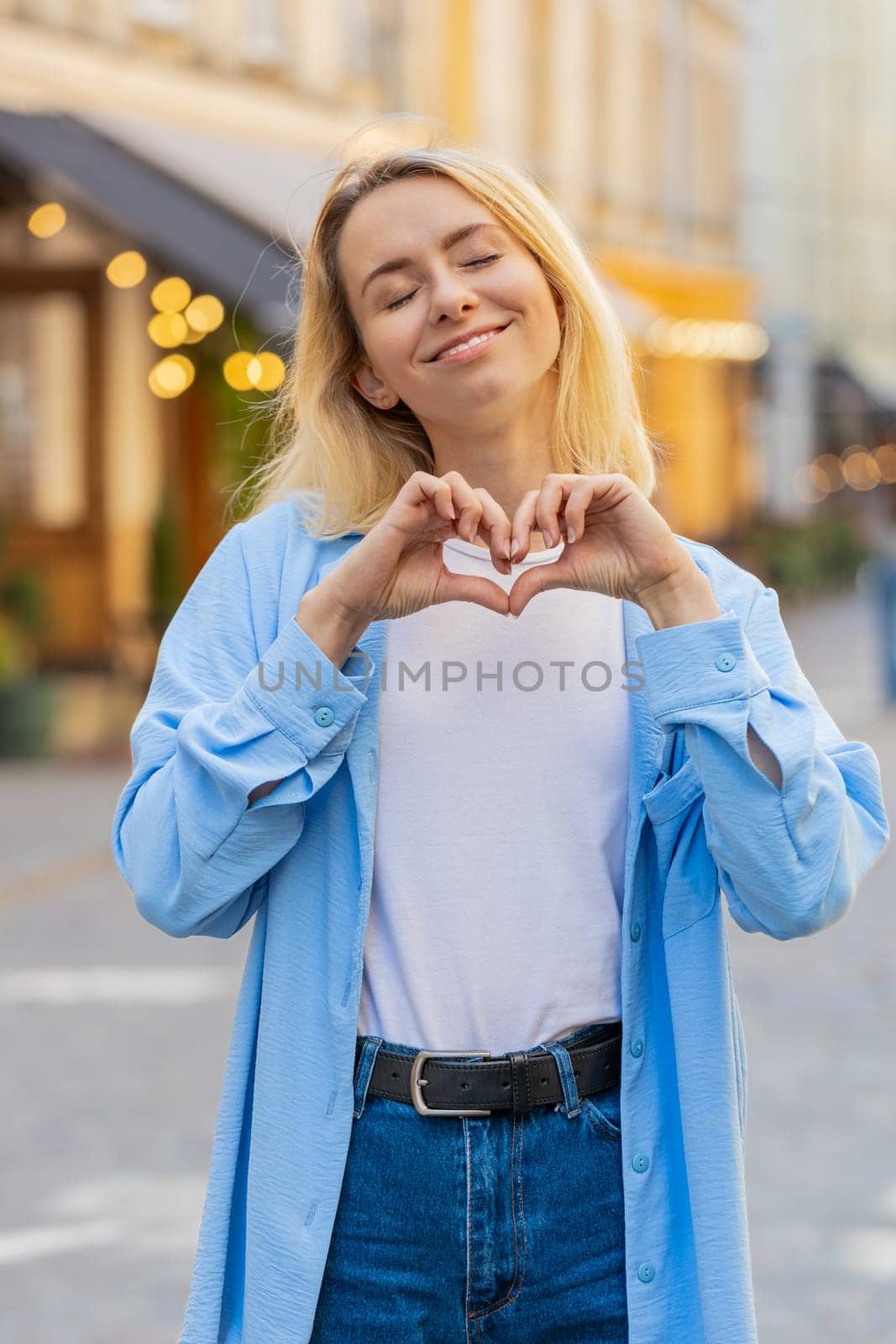 I love you. Caucasian woman makes symbol of love, showing heart sign to camera, express romantic feelings express sincere positive feelings. Charity, gratitude, donation. Outdoors in urban city street