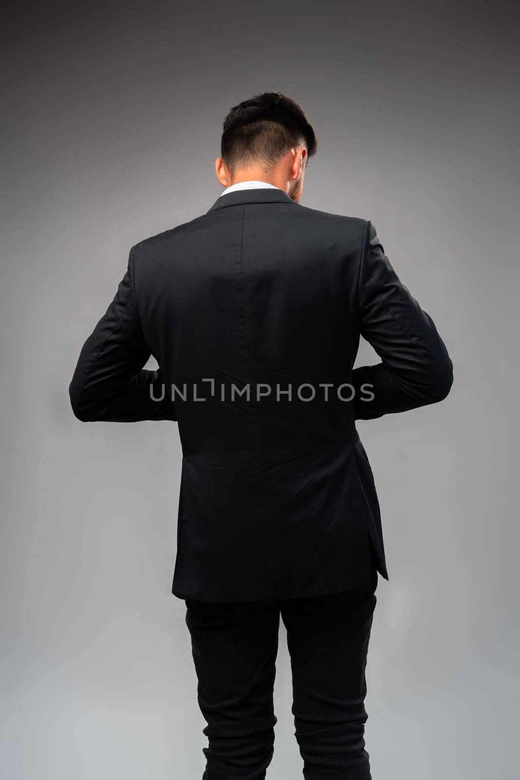 Young businessman from the back standing on gray background in studio