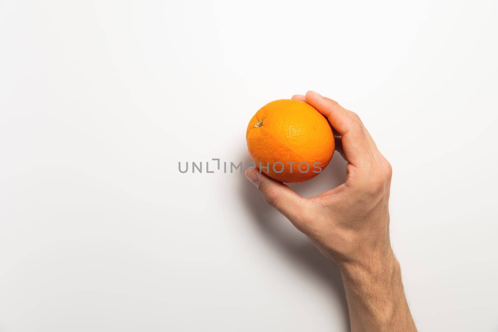 A man holding one orange in his hand on a white background. Top view, close-up. Healthy eating or organic food concept.