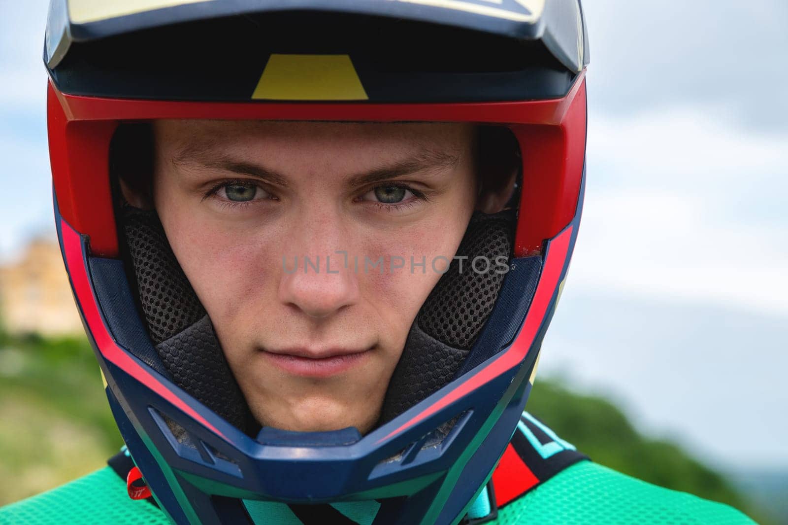 Close-up portrait of a confident handsome young athlete wearing a stylish helmet looking at the camera with eyes full of determination, ready to race on a summer day outdoors.