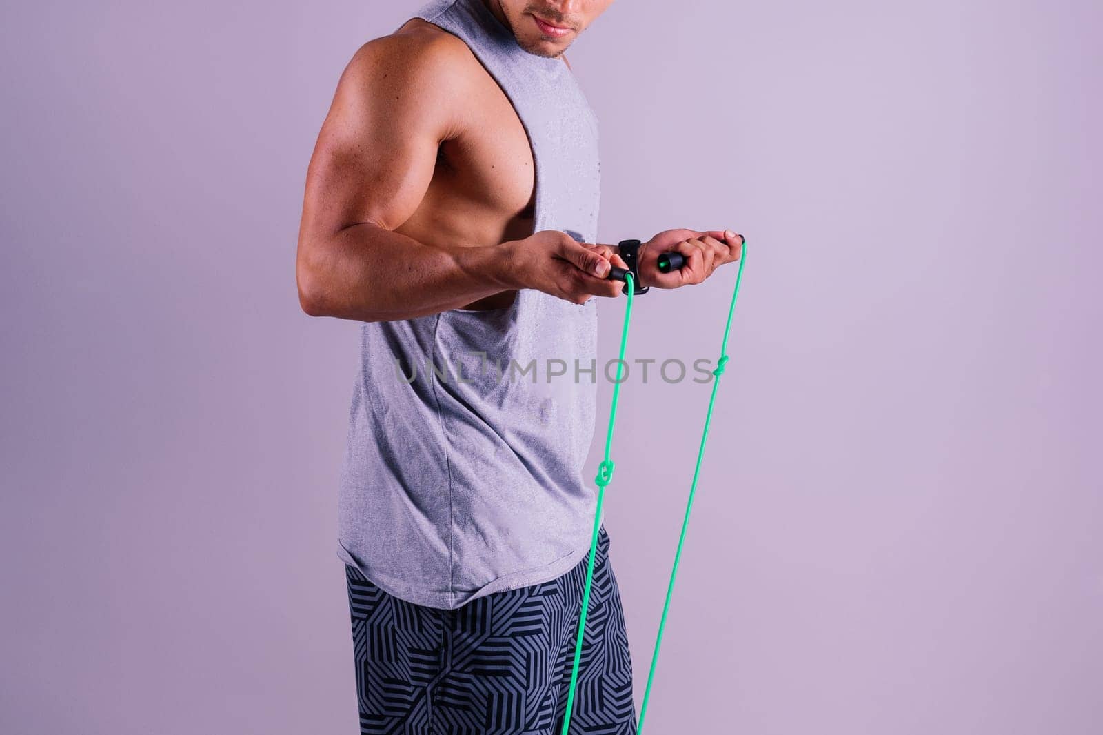 Man in grey tank top holds green jump rope with wrist by Zelenin