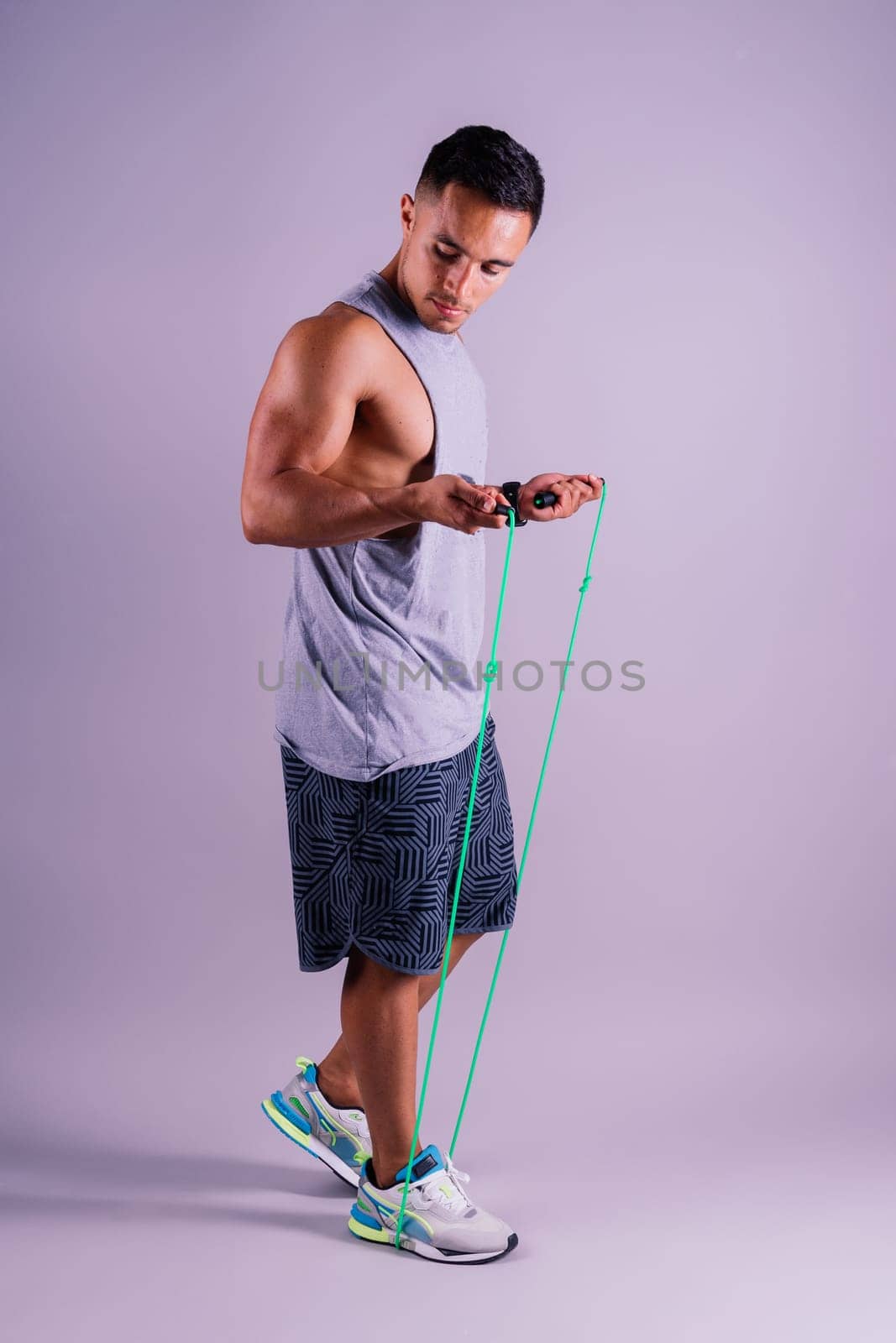 Man in grey tank top holds green jump rope with wrist by Zelenin