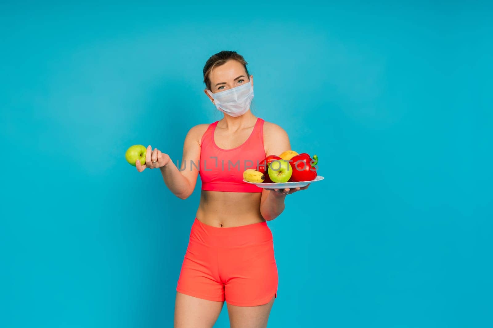 Woman in a face protection mask and fitness wear isolated over blue background.