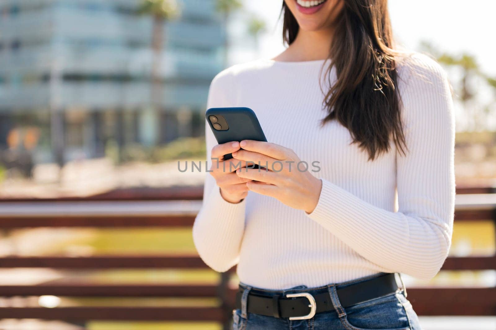 unrecognizable young caucasian woman using mobile phone outdoors, concept of technology of communication and modern lifestyle, copy space for text