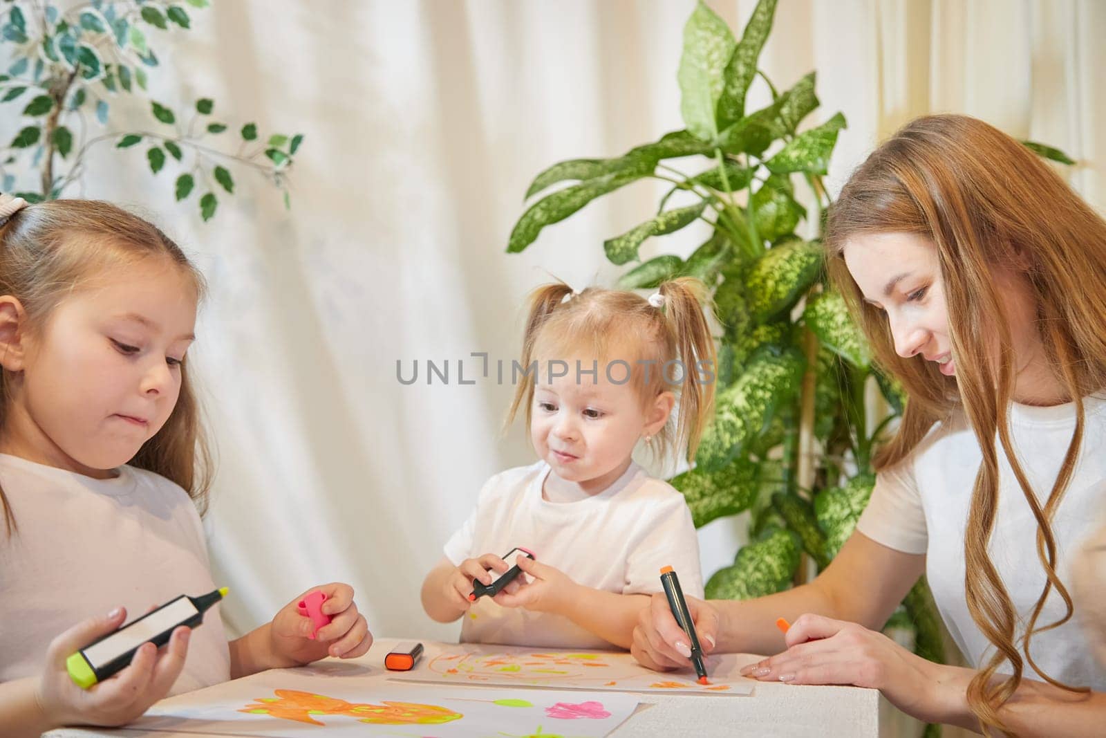 Young mother or babysitter, little daughter, sister teenager girl drawing at table in room. Painting, doing homework. Family enjoying leisure at home