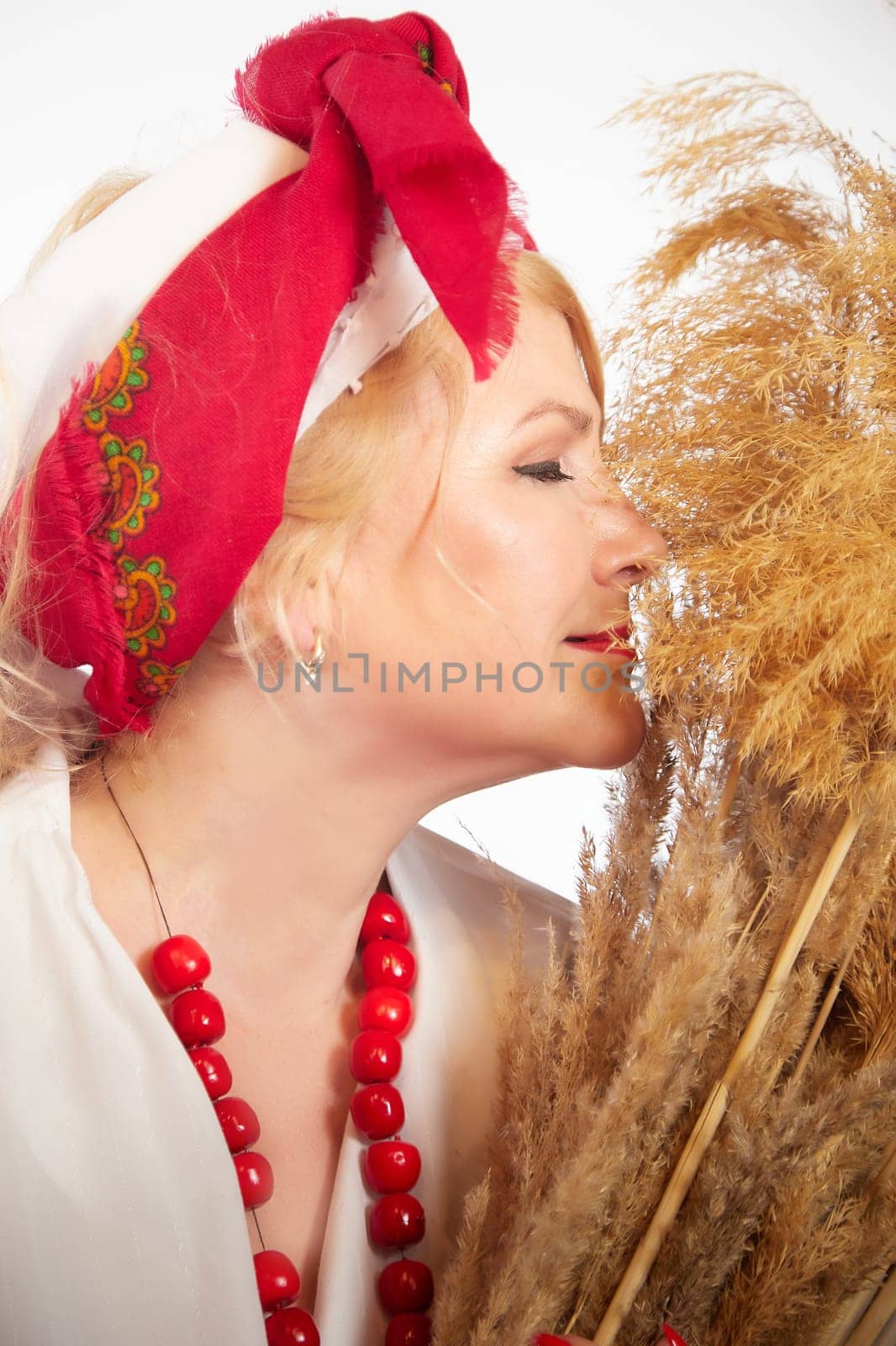 Portrait of heerful funny adult mature woman solokha with sheaf of ears. Female model in clothes of national ethnic Slavic style. Stylized Ukrainian, Belarusian or Russian woman in comic photo shoot by keleny