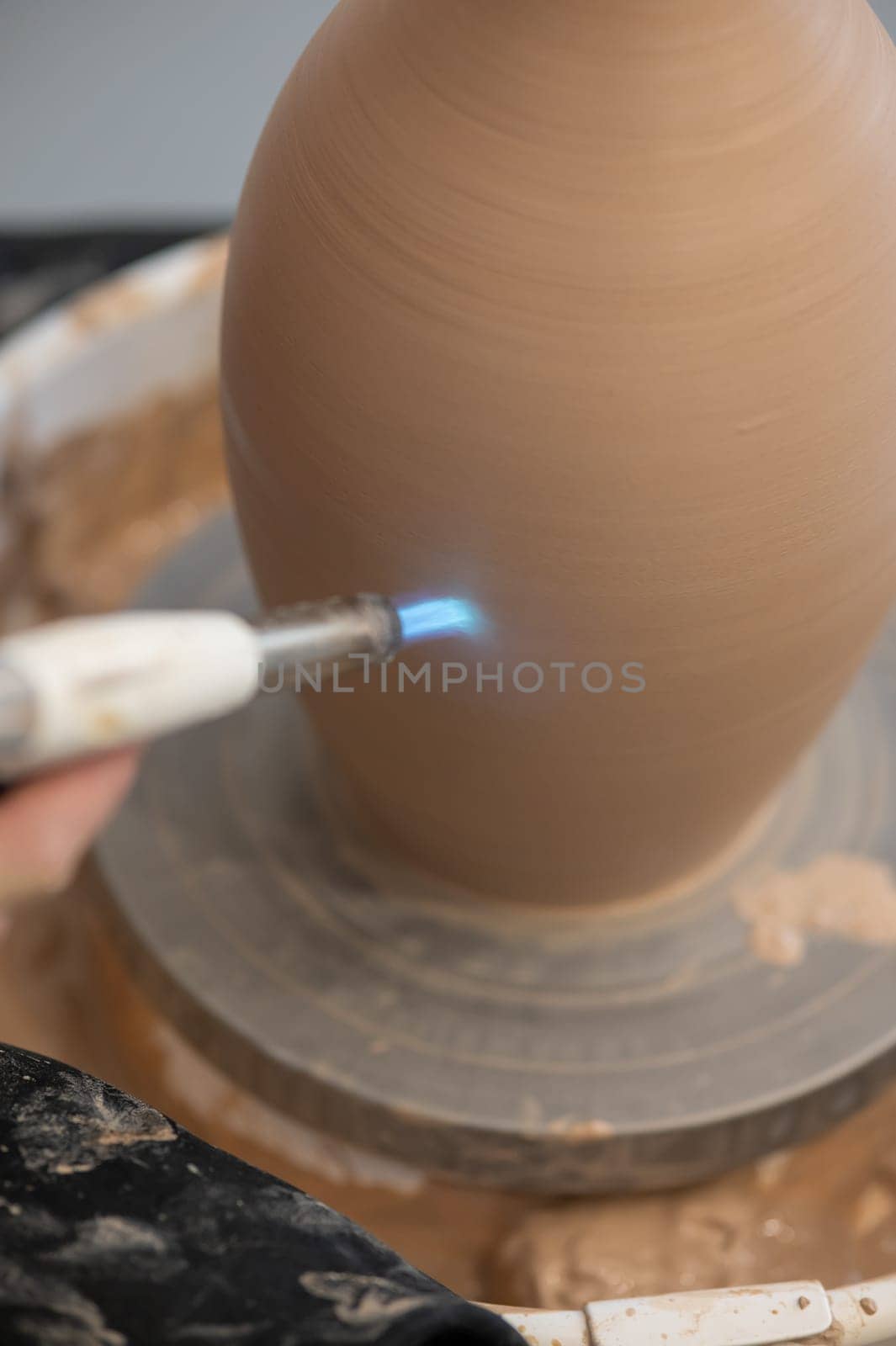 Close-up of a potter's hands firing a jug with a gas burner on a potter's wheel. Vertical photo