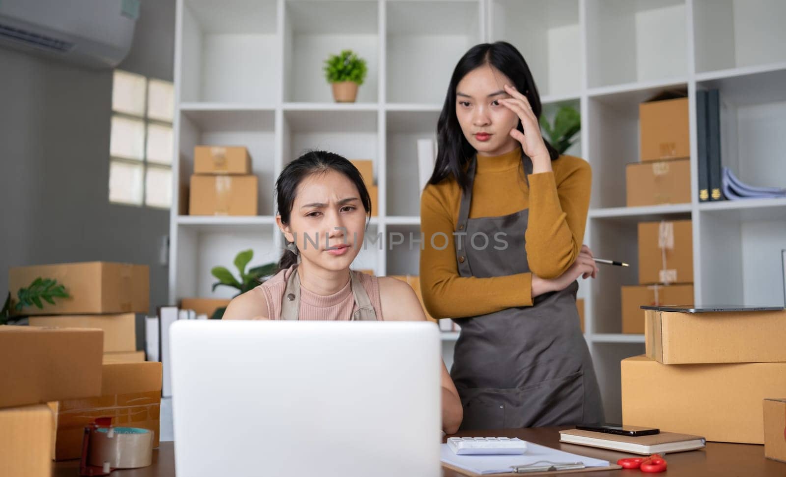 Two young Asian women who are worried Was stressed while running a small business together having trouble selling products online using a laptop..