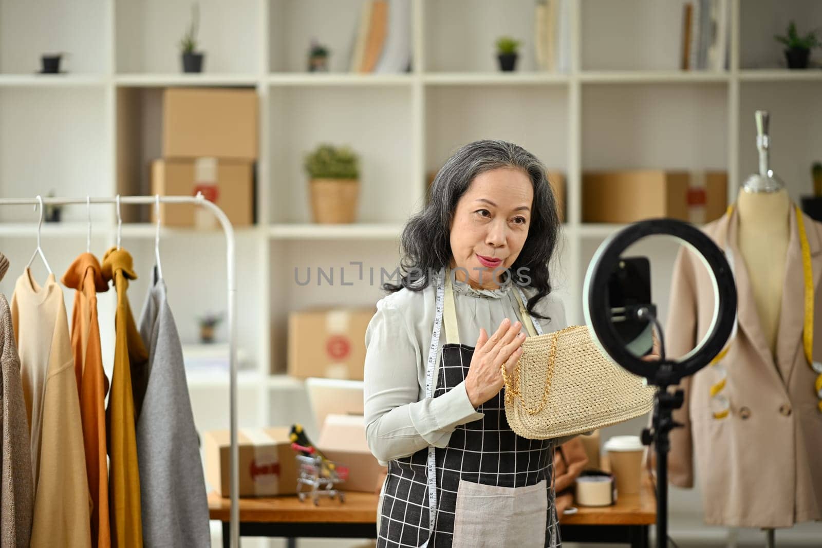 Confident senior business owner live streaming to sale clothes product to customers at her clothing shop.