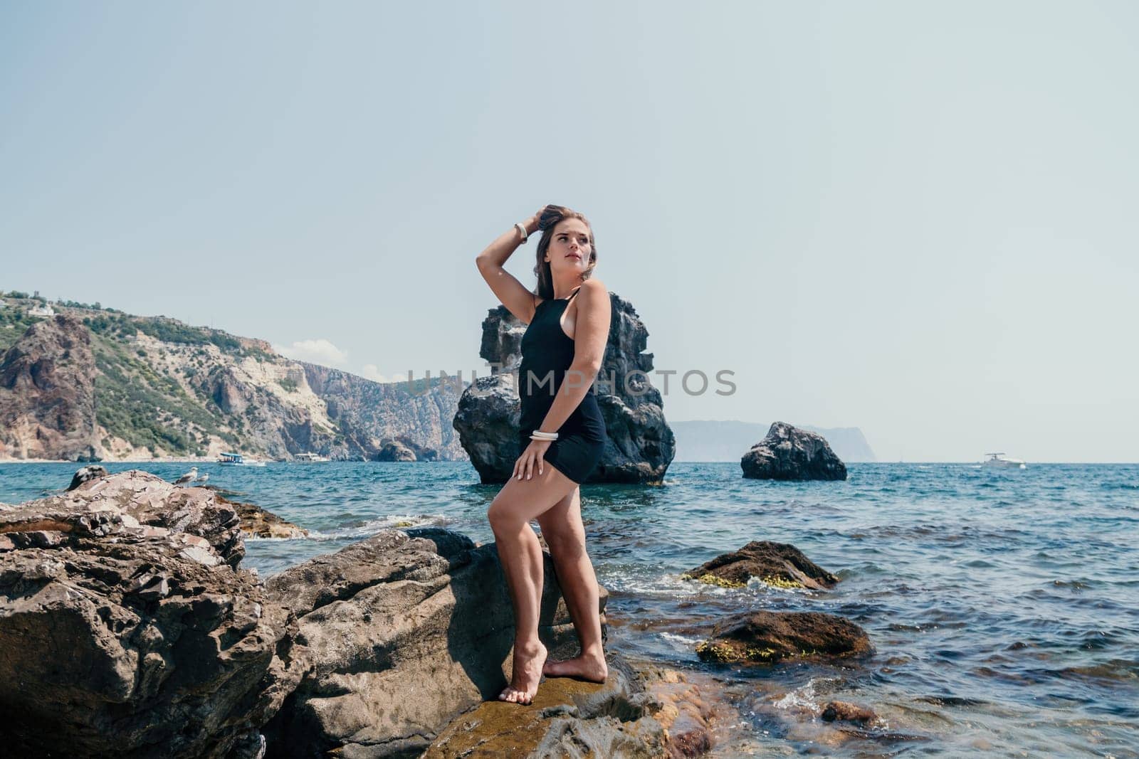 Woman travel sea. Young Happy woman in a long red dress posing on a beach near the sea on background of volcanic rocks, like in Iceland, sharing travel adventure journey