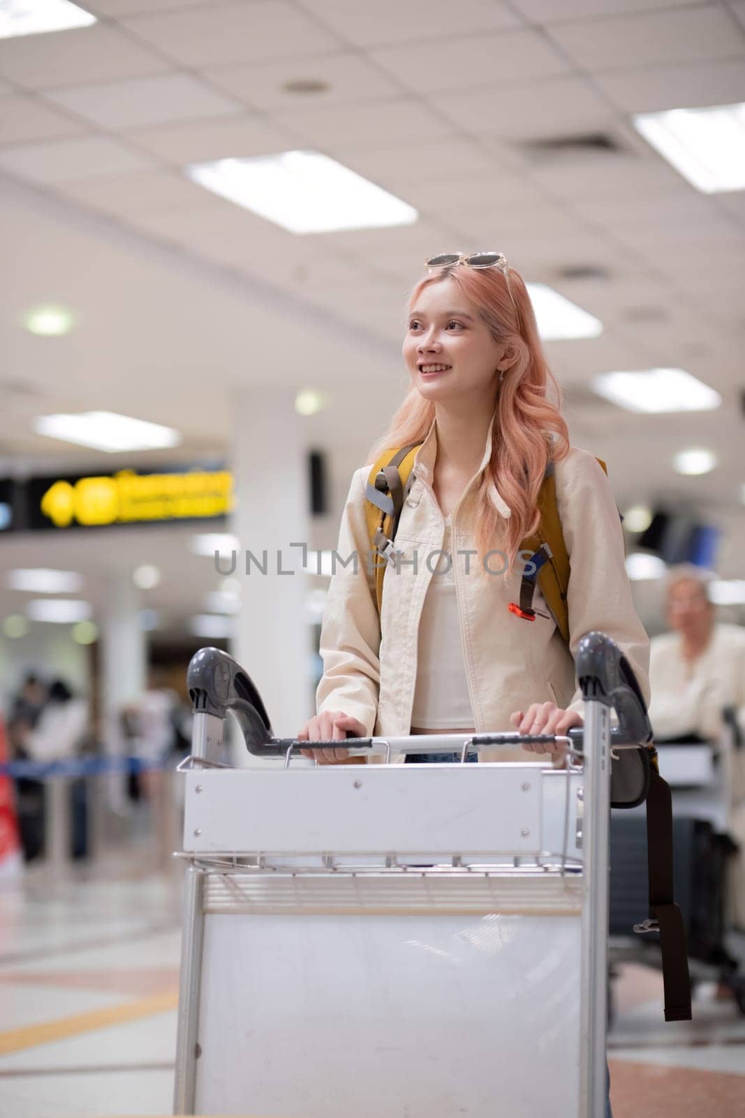 Young traveler with luggage cart and backpack at airport terminal. Concept of travel, exploration, and excitement.