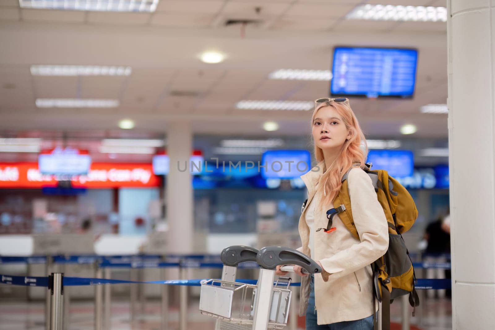 Young traveler with luggage cart and backpack at airport terminal. Concept of travel, exploration, and excitement.