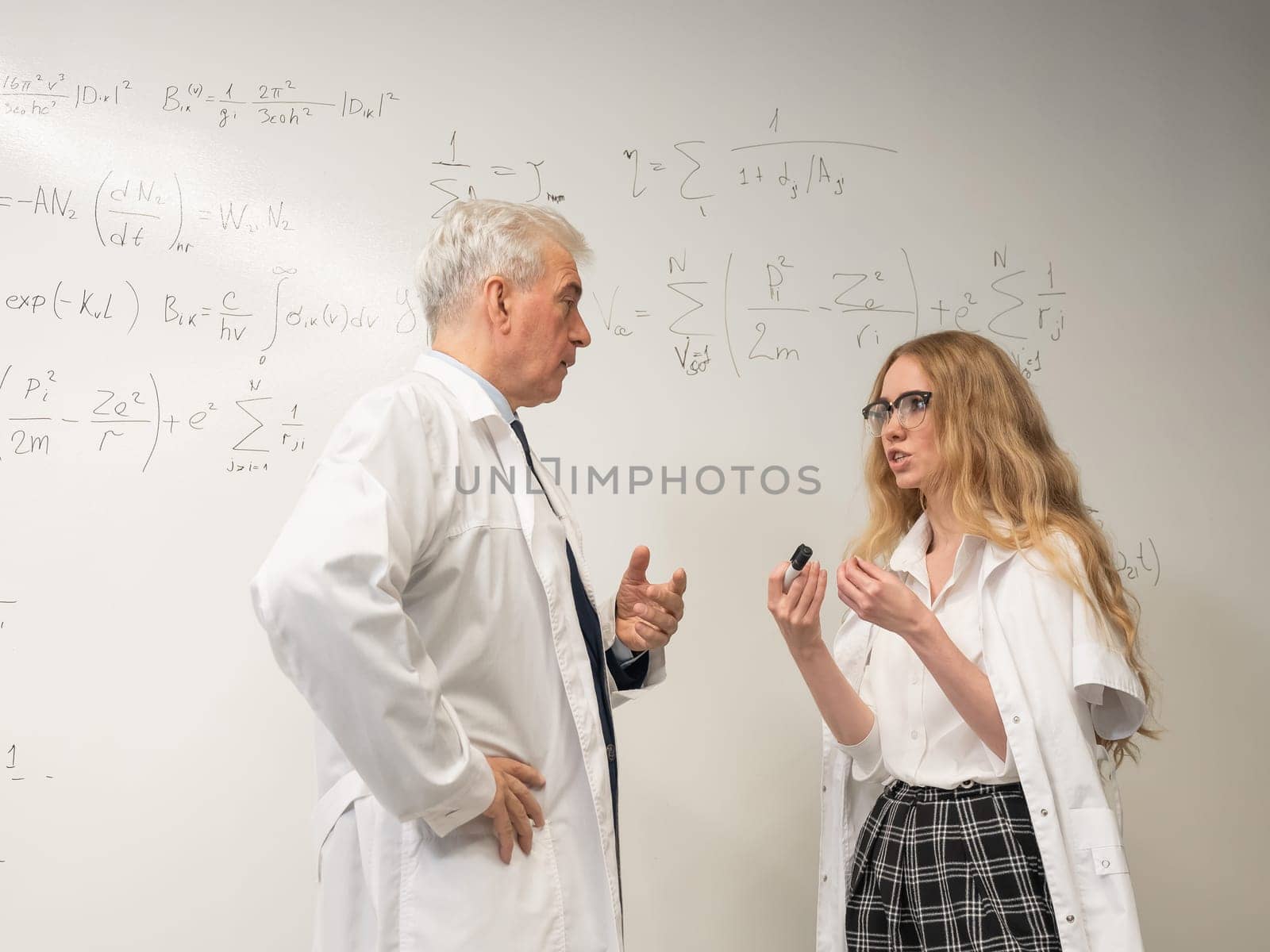 An elderly man and a young woman at a white board. Colleagues scientists discuss work issues