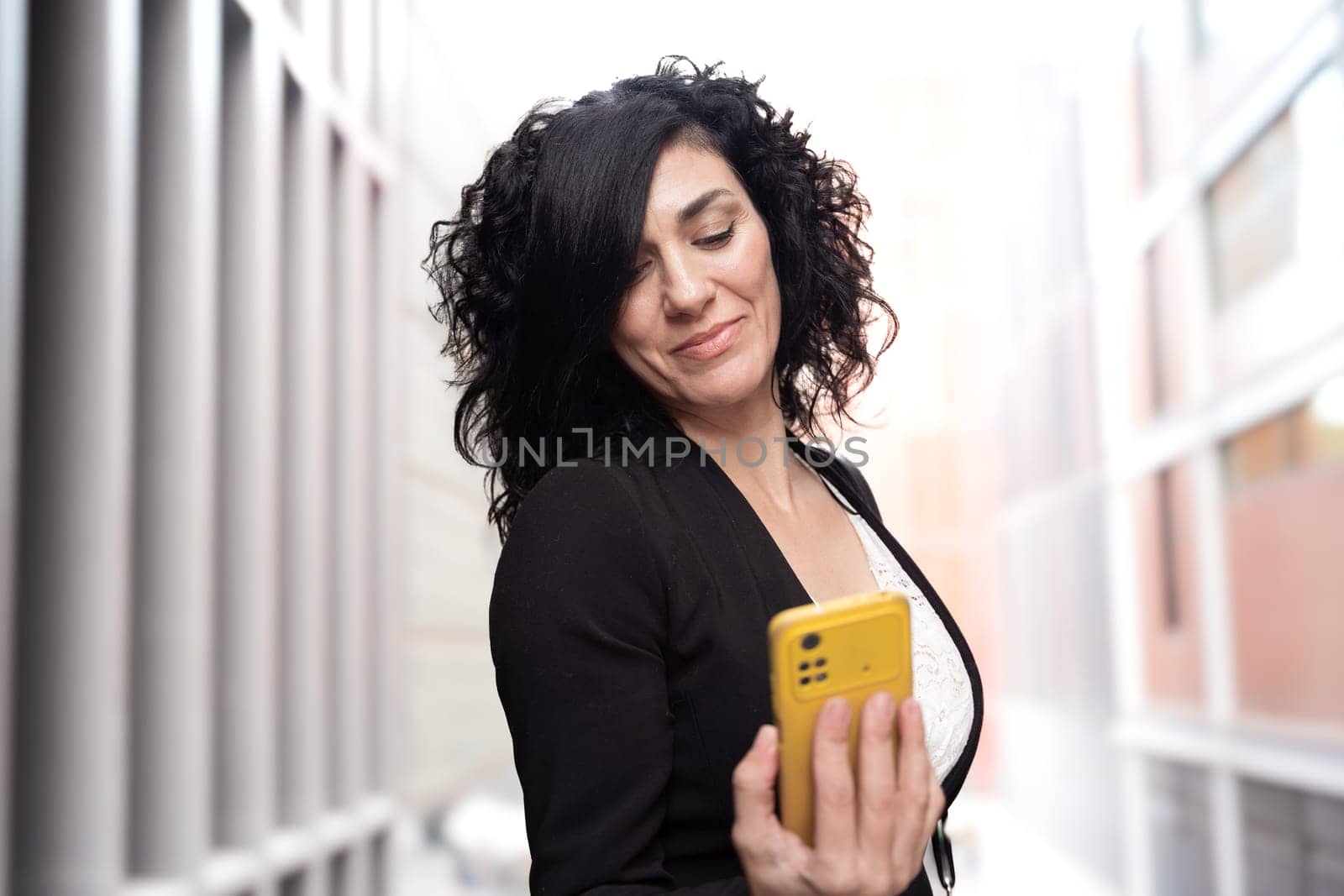 Young woman with cell phone in hands, writes messages and reads news online, using an app with a gesture of happiness.