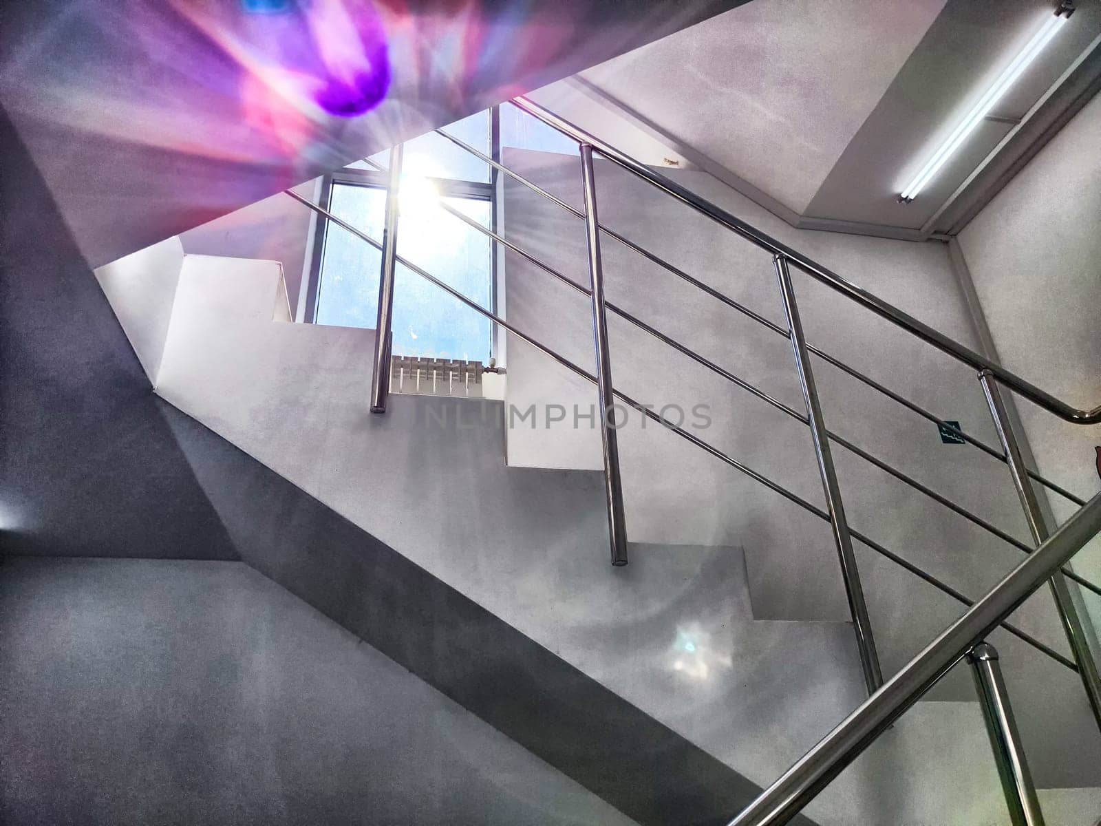A bright staircase with metal railings and sunlight streaming through a window, creating sun flare