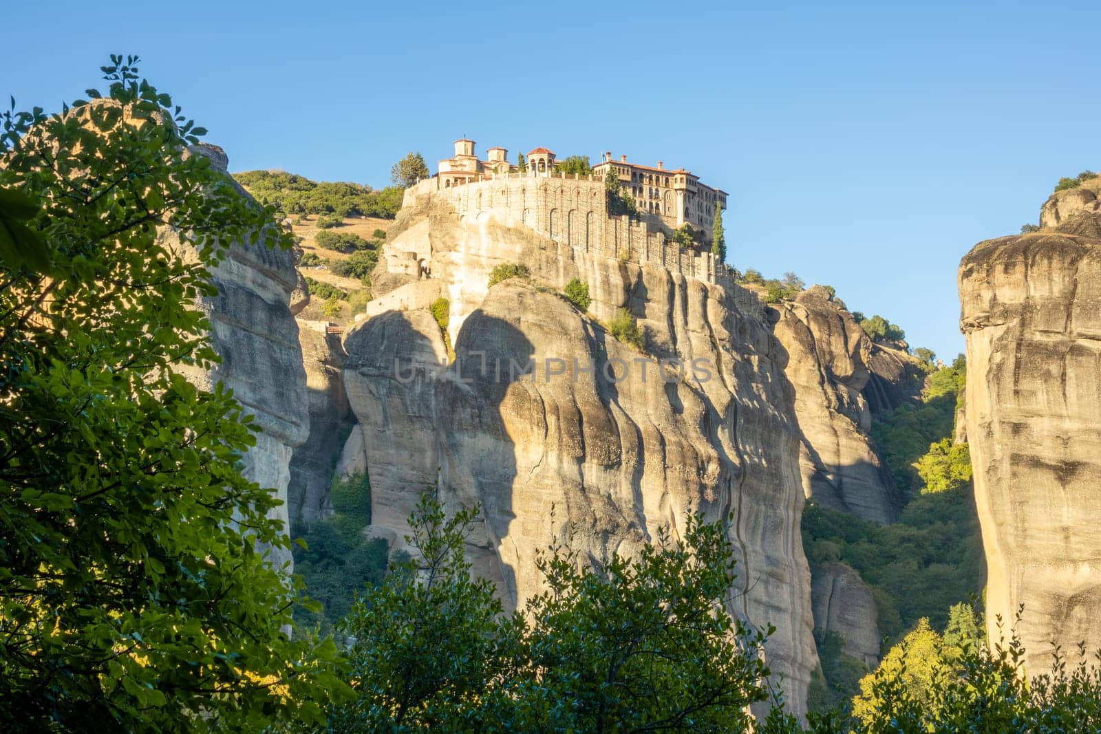 Greece. Sunny summer day in Meteora. Large rock monastery near a green hill against a blue sky