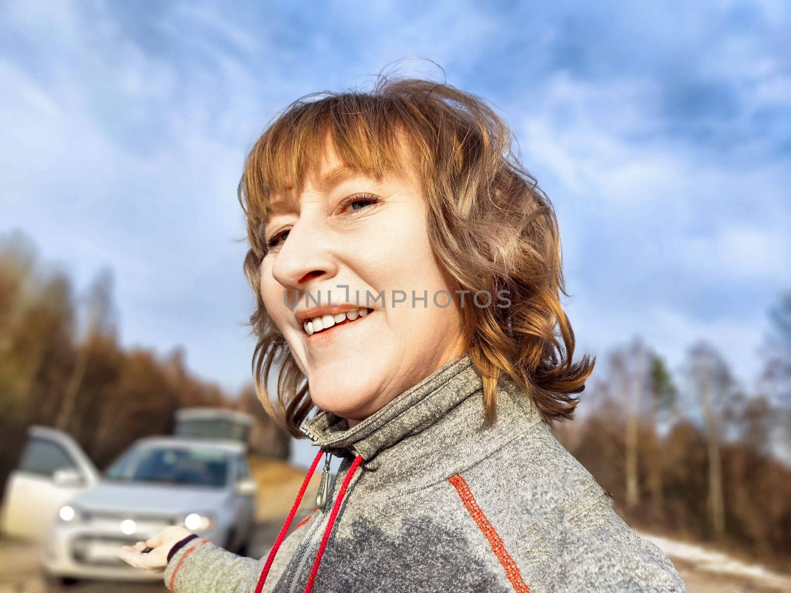 A woman takes a selfie on the road near a car. The concept of car travel. A woman captures a selfie with her car in the background during road trip