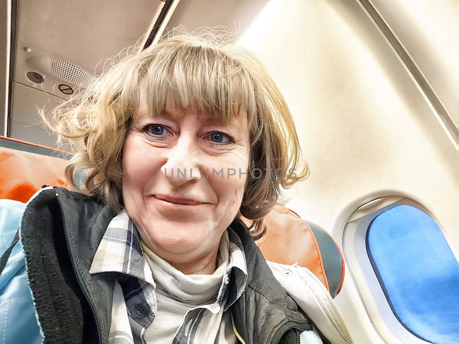 A middle-aged woman takes a selfie on a plane. Portrait of a girl. Smiling Woman on Airplane