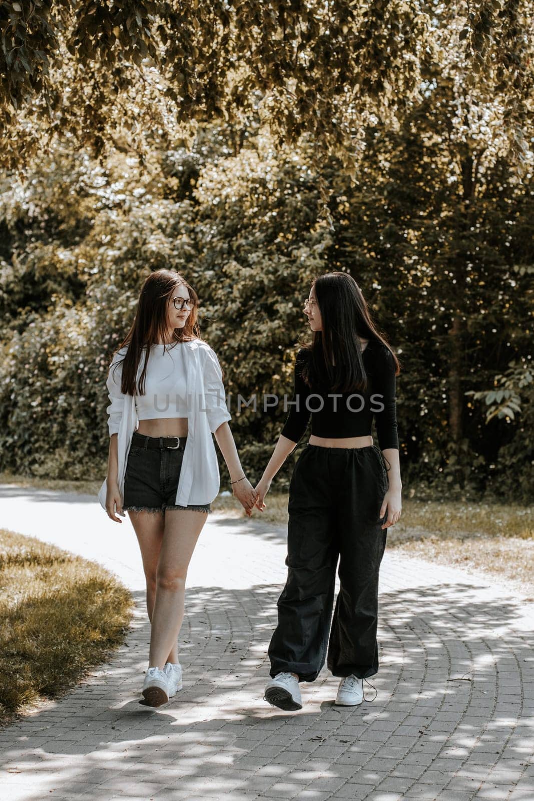 Portrait of two beautiful Caucasian girls walking in the park. by Nataliya