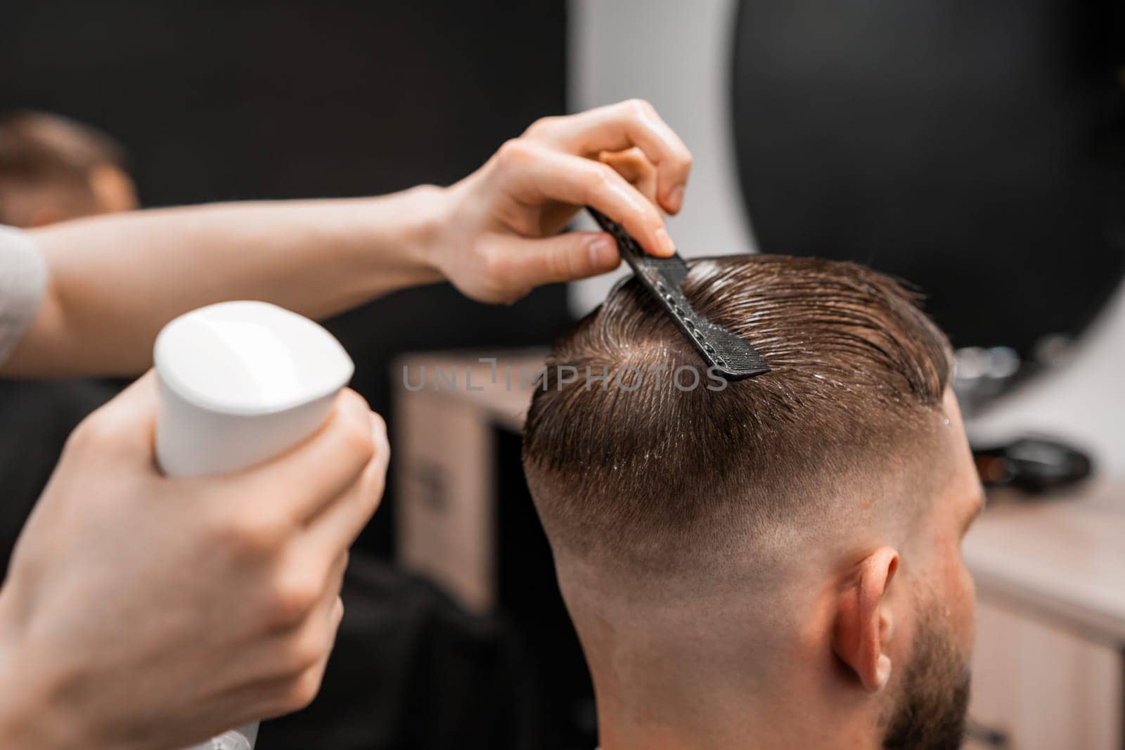 A barber sprays and combs mans hair at the barbershop.