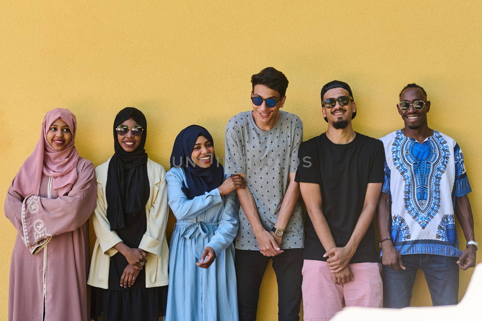 A diverse group of African-American and Middle Eastern teenagers stand confidently in front of a vibrant yellow wall, showcasing unity and urban style