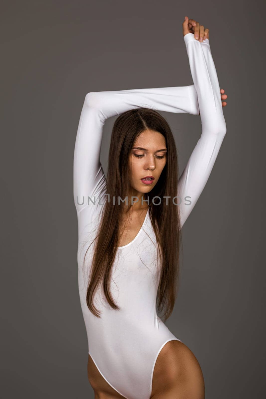 Slim tanned beautiful perfect woman in white bodysuit on gray background.