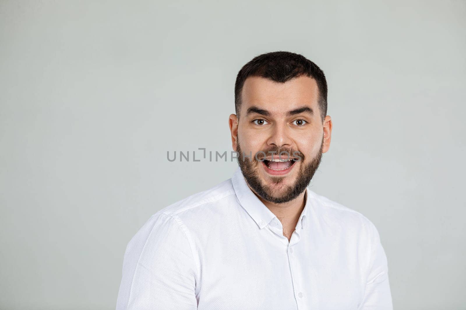 Portrait of young surprised handsome bearded man with shocked facial expression on gray background