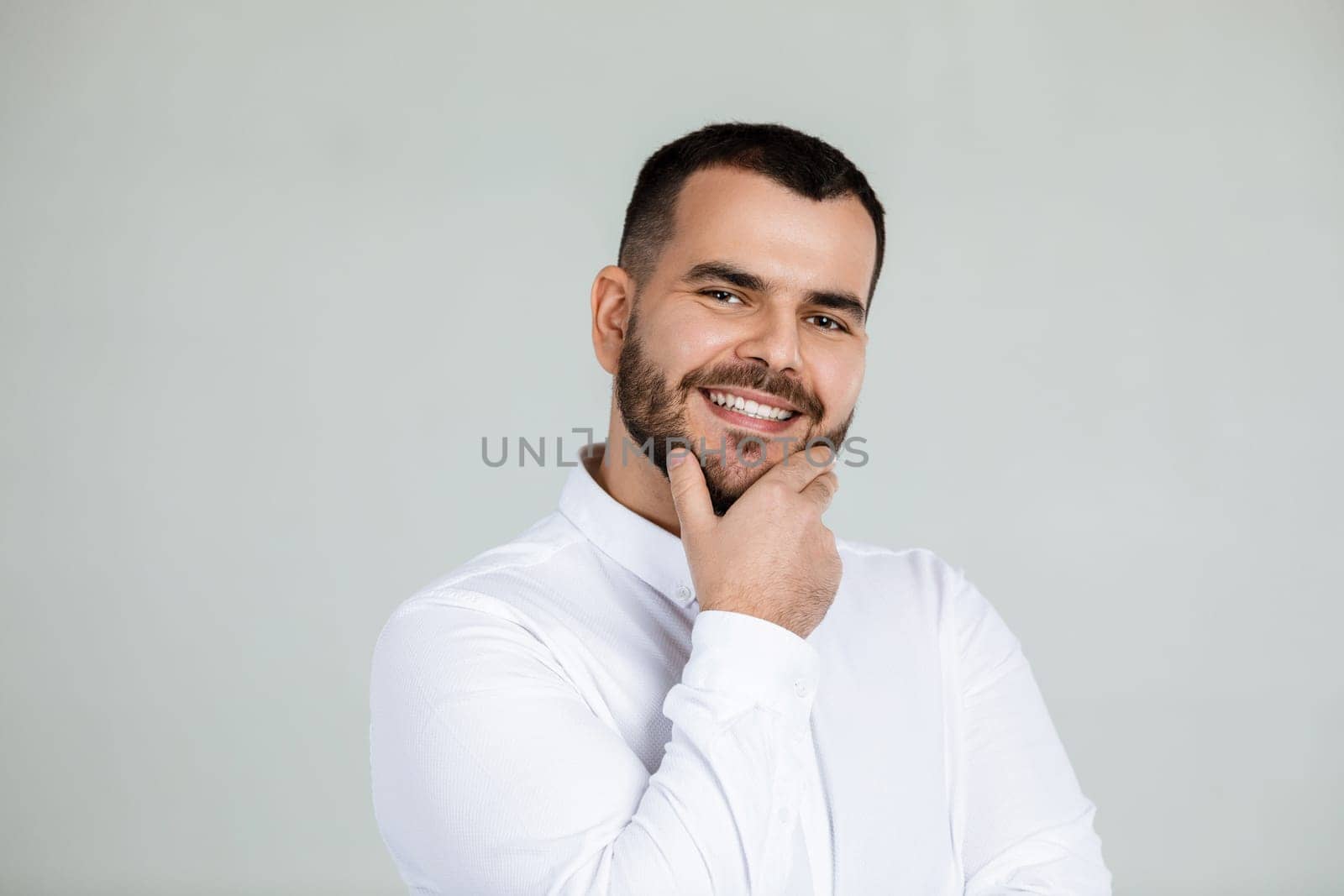 Close-up portrait of smiling handsome bearded man looking at camera on gray background