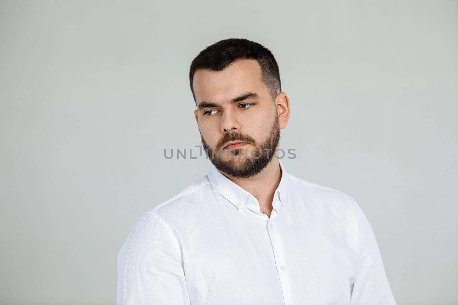 portrait of sad bearded man in white shirt on gray background