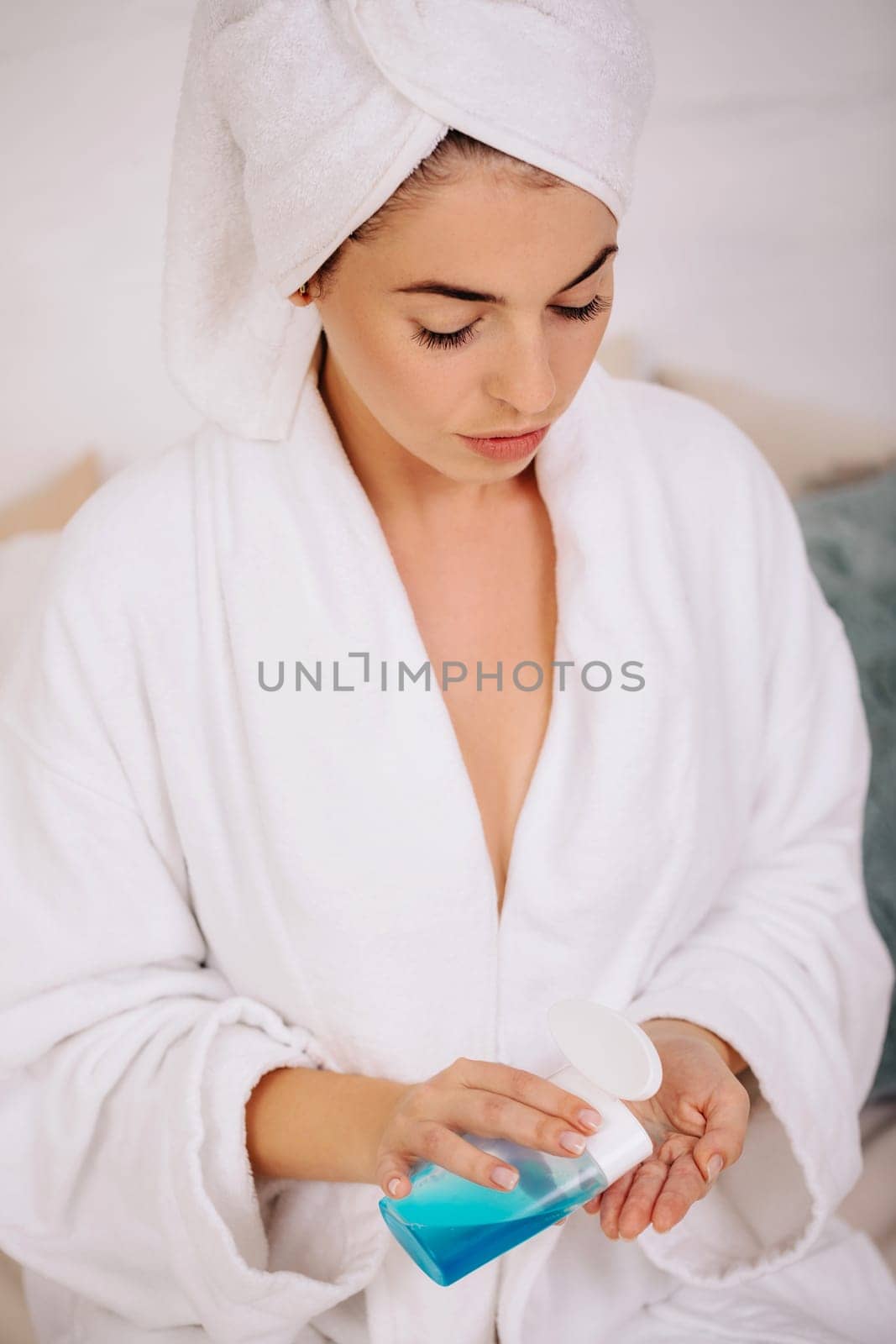 beautiful woman in bathrobe and towel uses tonic or lotion product. girl holding skin cleansing, close-up
