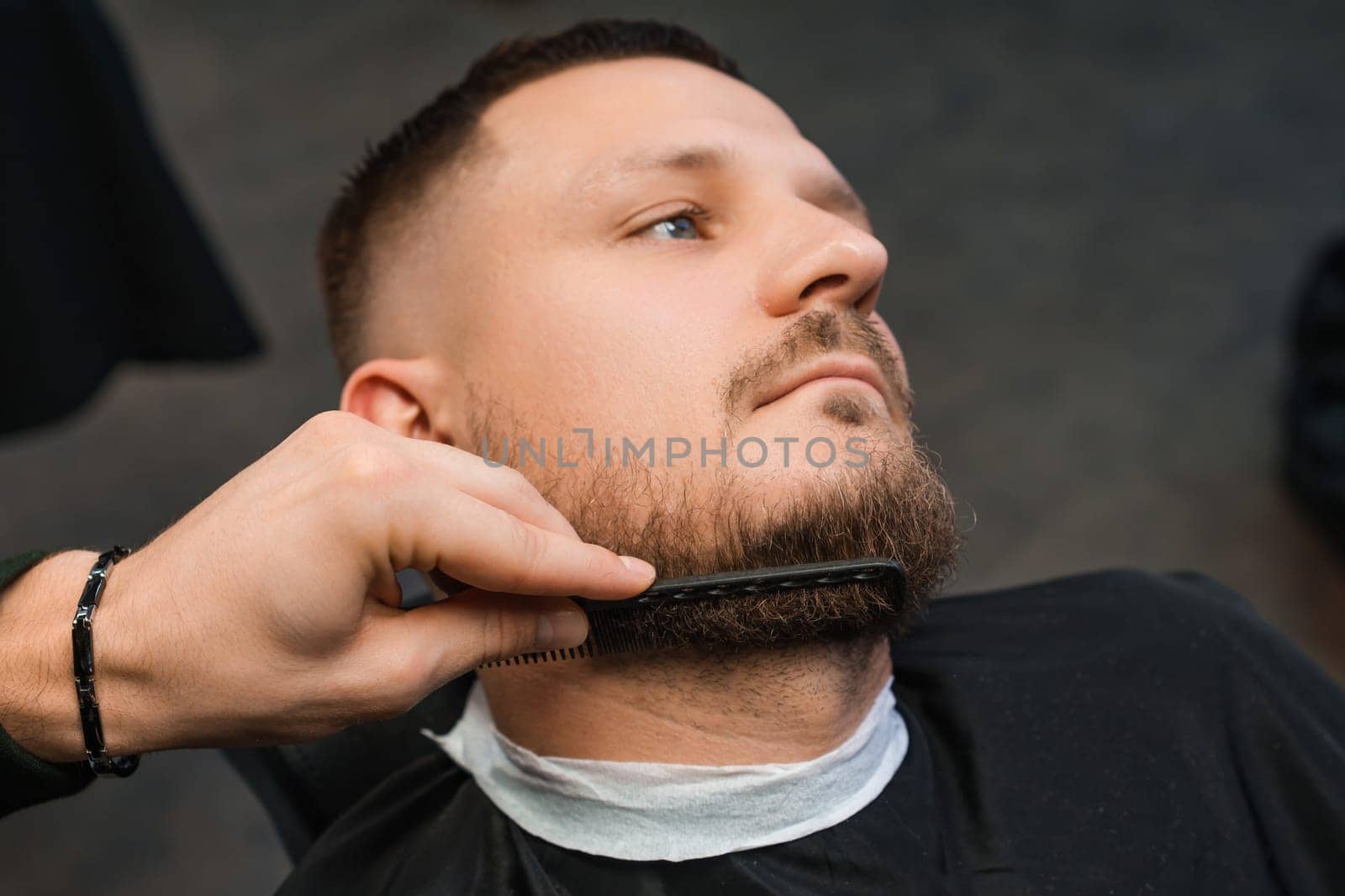 Barber combing clients beard in the barbershop.