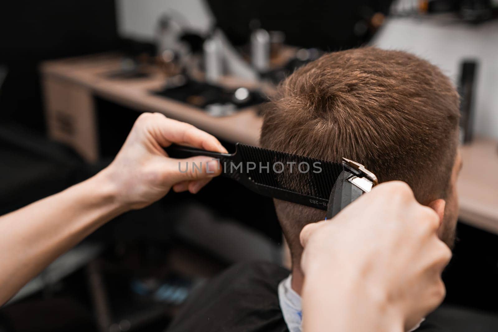 The client gets their hair shaved with an electric trimmer by the barber in a barbershop.