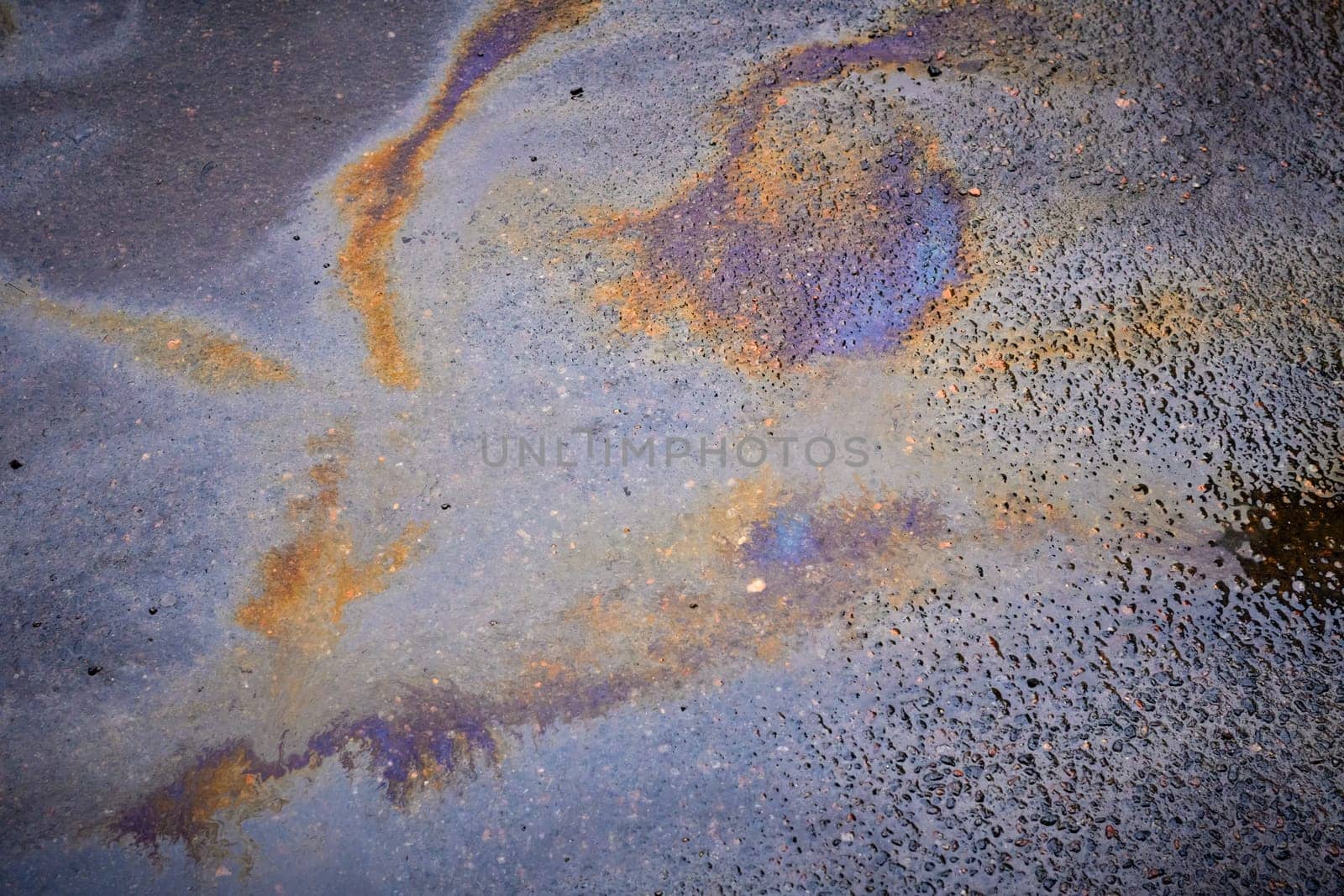Colorful rainbow stains of an oil spill on wet asphalt.