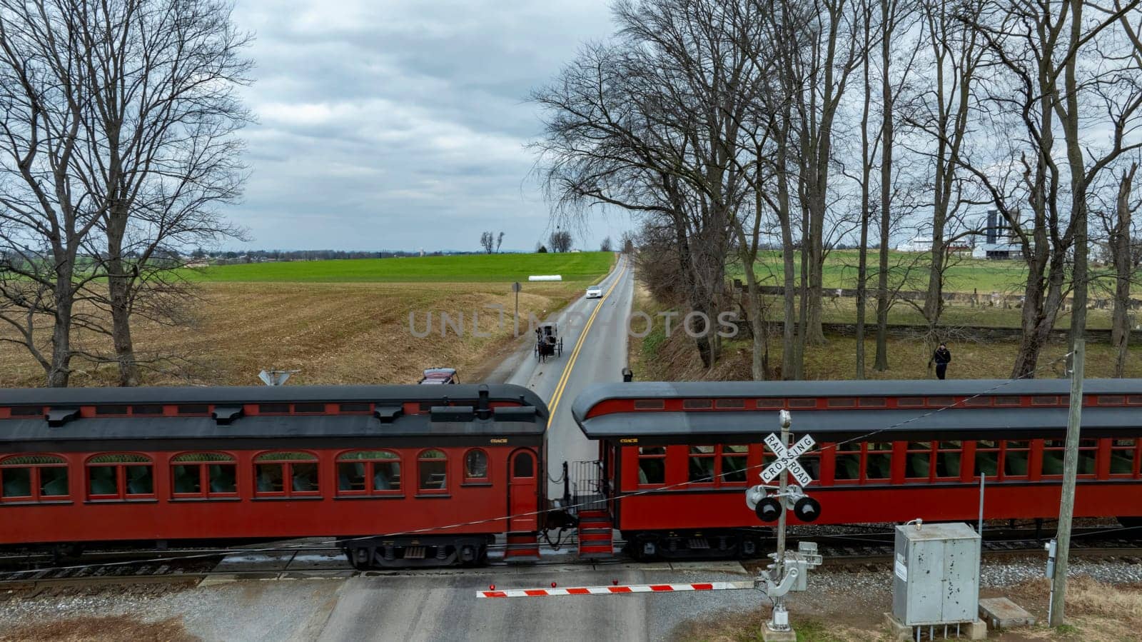 A Historic Train Crossing Rural Road with an Amish Horse-Drawn Carriage