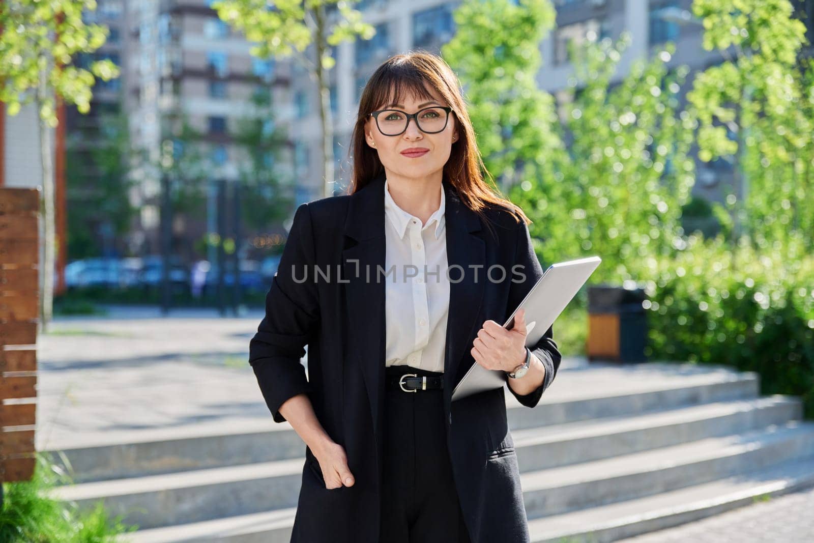 Middle-aged business woman in suit with laptop, near outdoor building. Female teacher posing near school educational center, office worker entrepreneur accountant economist banker financier lawyer