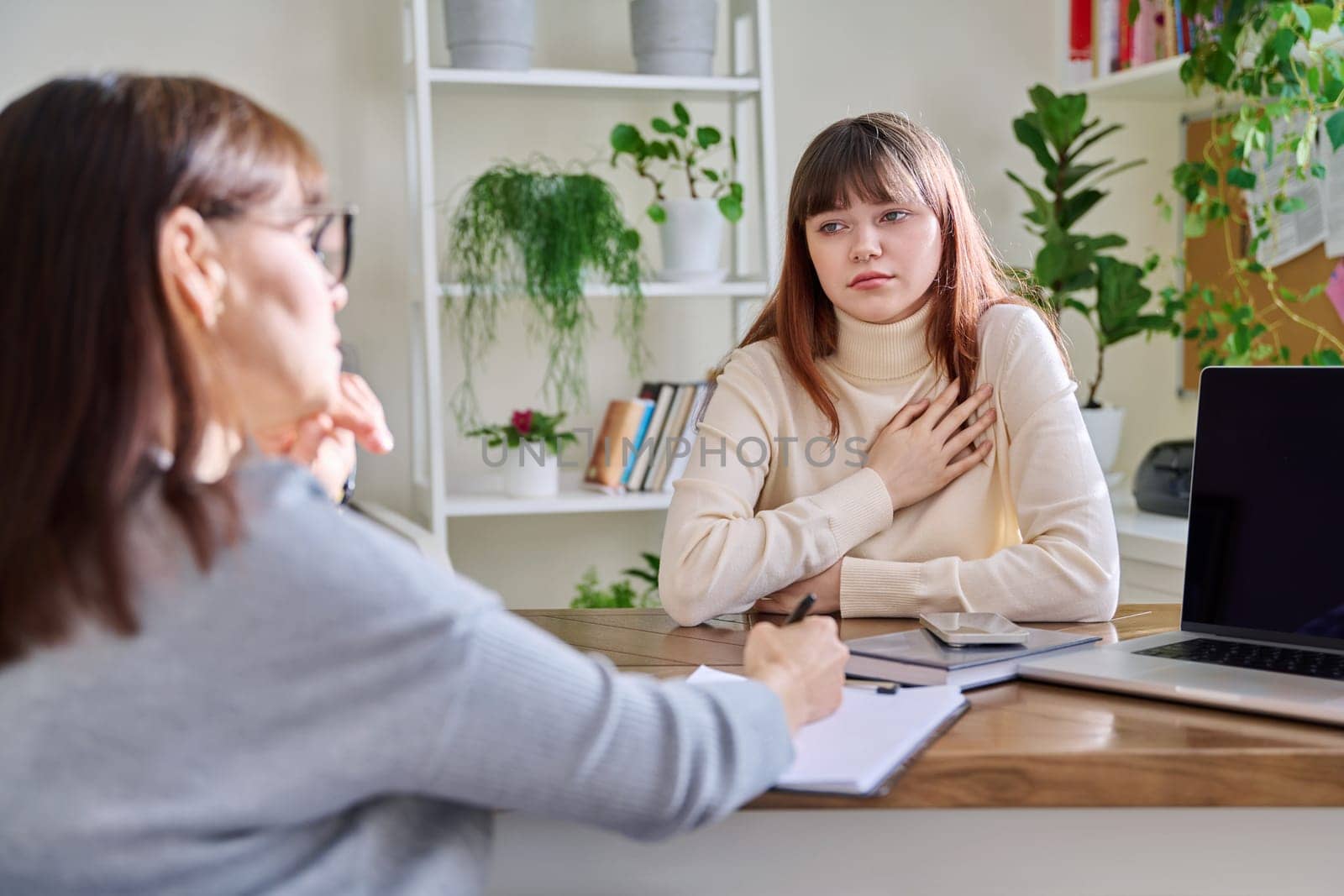 Sad upset teenage girl talking to psychotherapist psychologist counselor at therapy session in specialist office. Mental health of youth, social services for mental support, psychological counseling