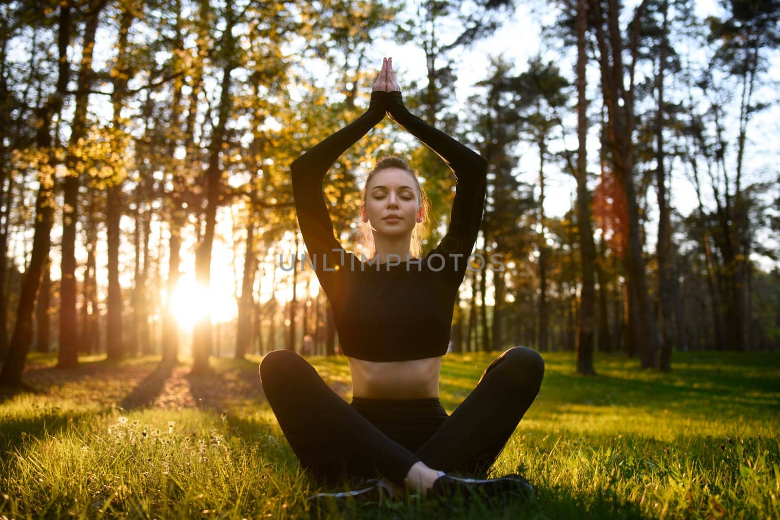 A woman practices yoga meditation at dawn in a peaceful forest, connecting with nature and serene surroundings