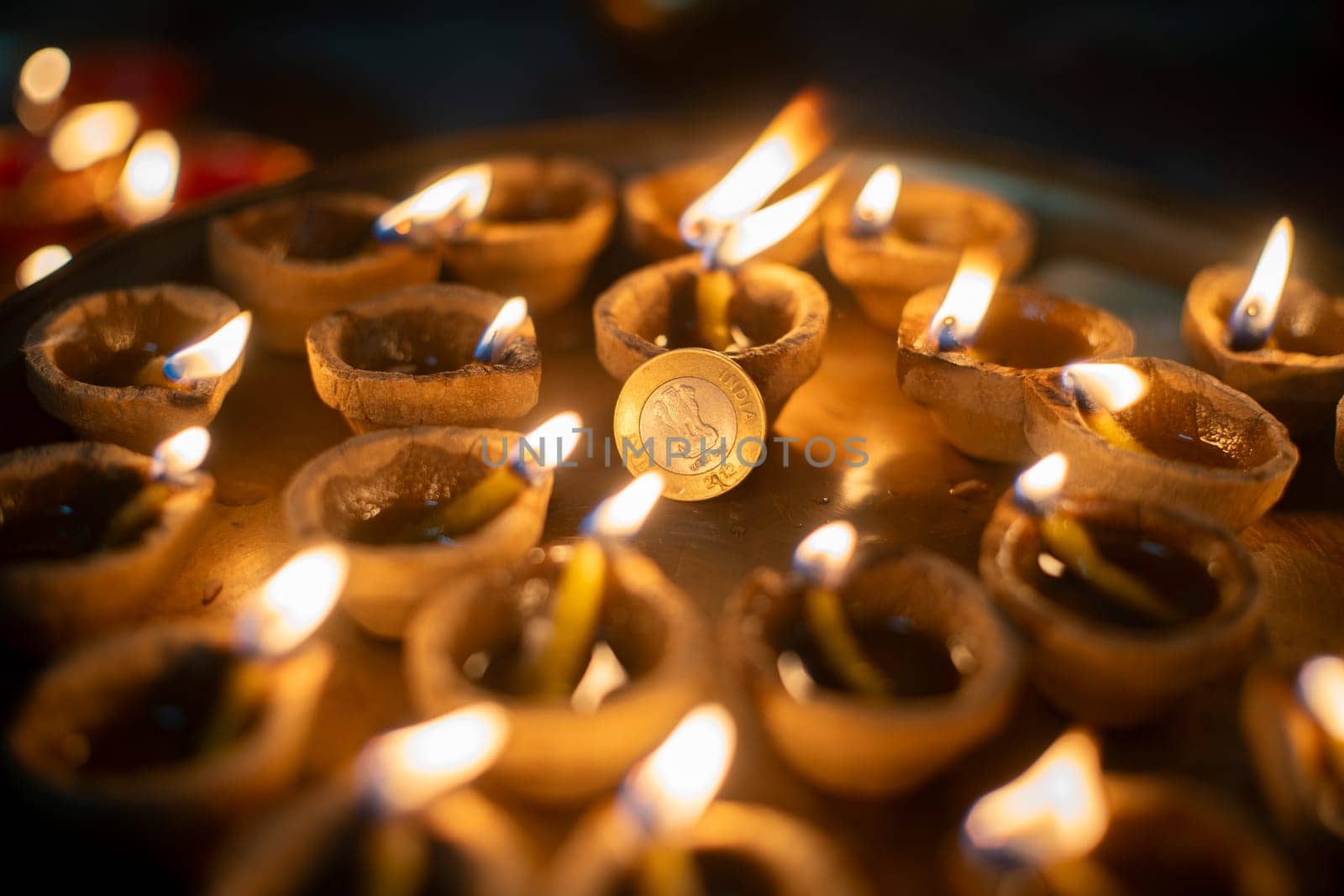 macro shot showing a circle of diya oil lamps around a rupee coin showing the offerings and prayers to the hindu wealth goddess lakshmi in India