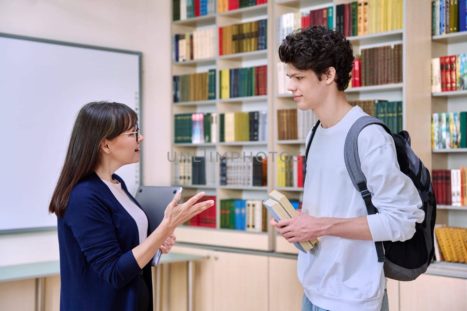 Female teacher talking to guy teenage college student inside educational library office by VH-studio