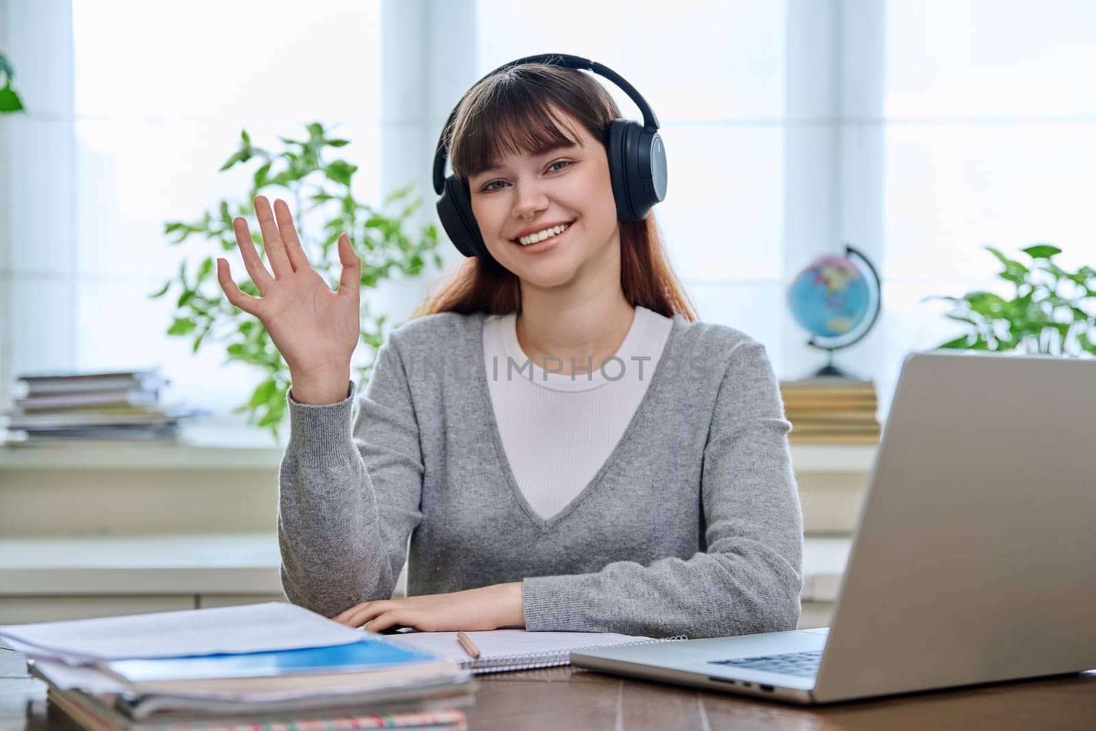 Portrait of teenage college student wearing headphones, sitting at desk, smiling and looking at camera. Education, training, youth 18,19, 20 years old