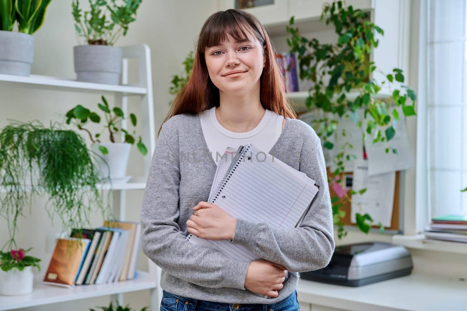 Portrait of smiling female student, 19,20 years old, looking at camera holding notebooks and textbooks, in home interior. Youth, lifestyle, education college university concept