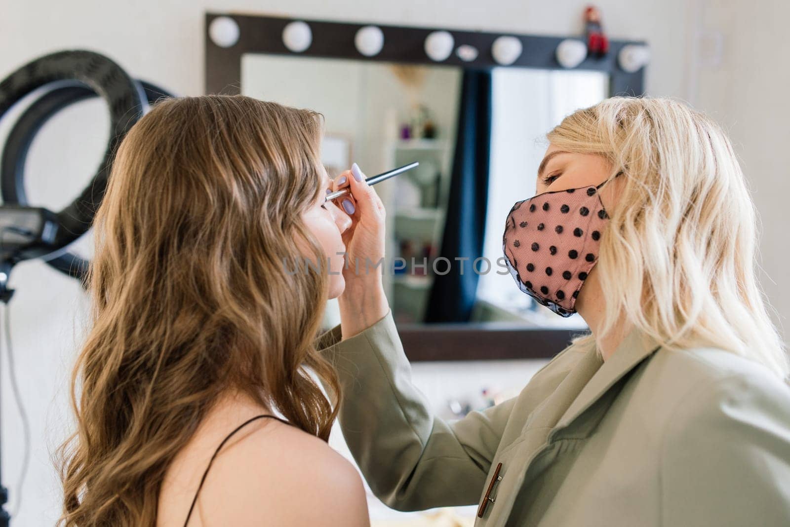 Backstage of photo shoot: Make-up artist applies makeup on beautiful white model.