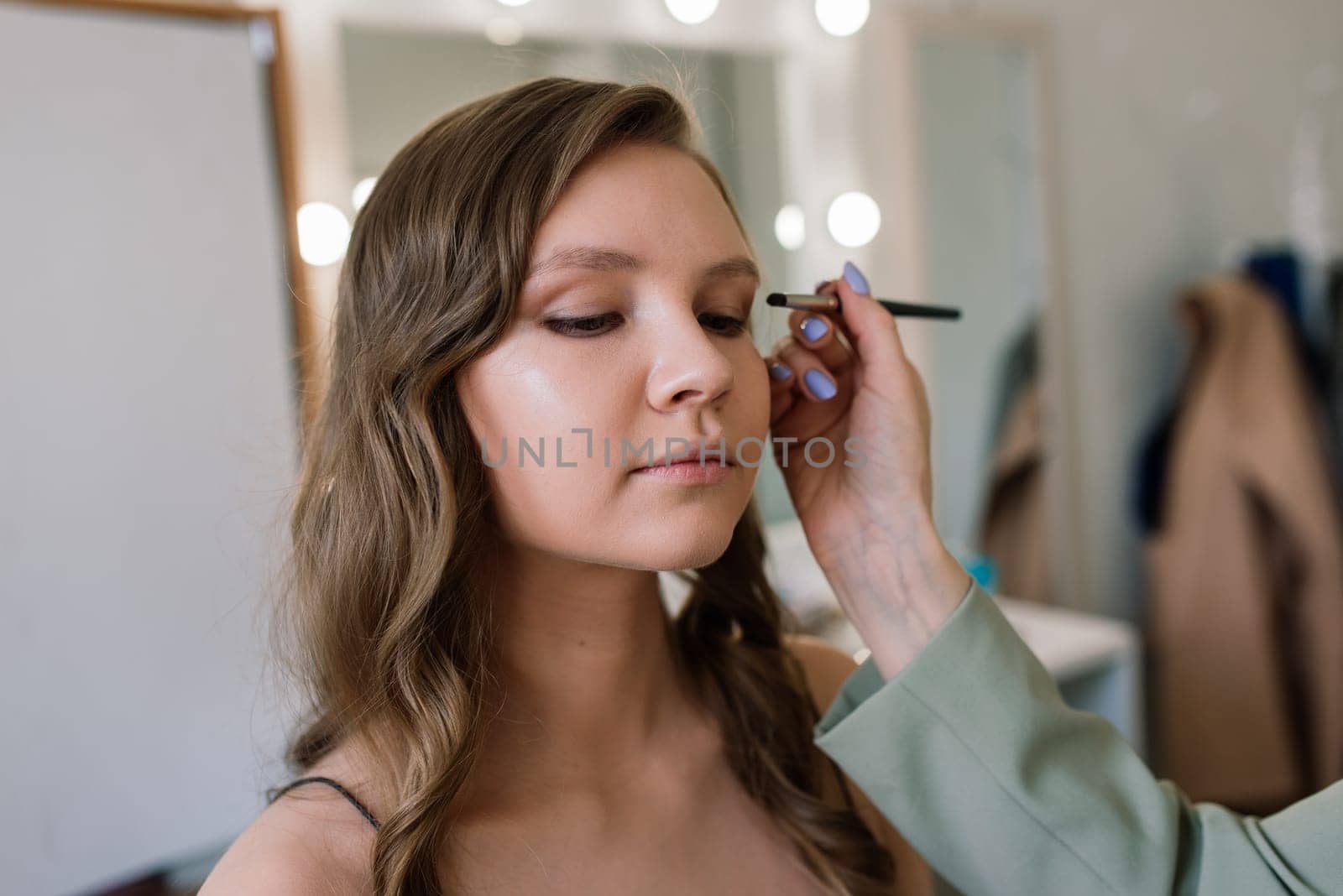 Backstage of the photo shoot: Make-up artist applies makeup on beautiful white model. by Zelenin