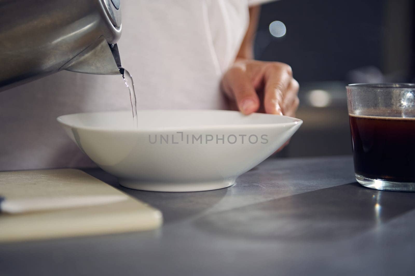 Close-up woman pouring boiled water from a teapot into a white bowl with oat flakes, preparing dry breakfast, standing t kitchen counter at home. Food and drink concept. Healthy eating