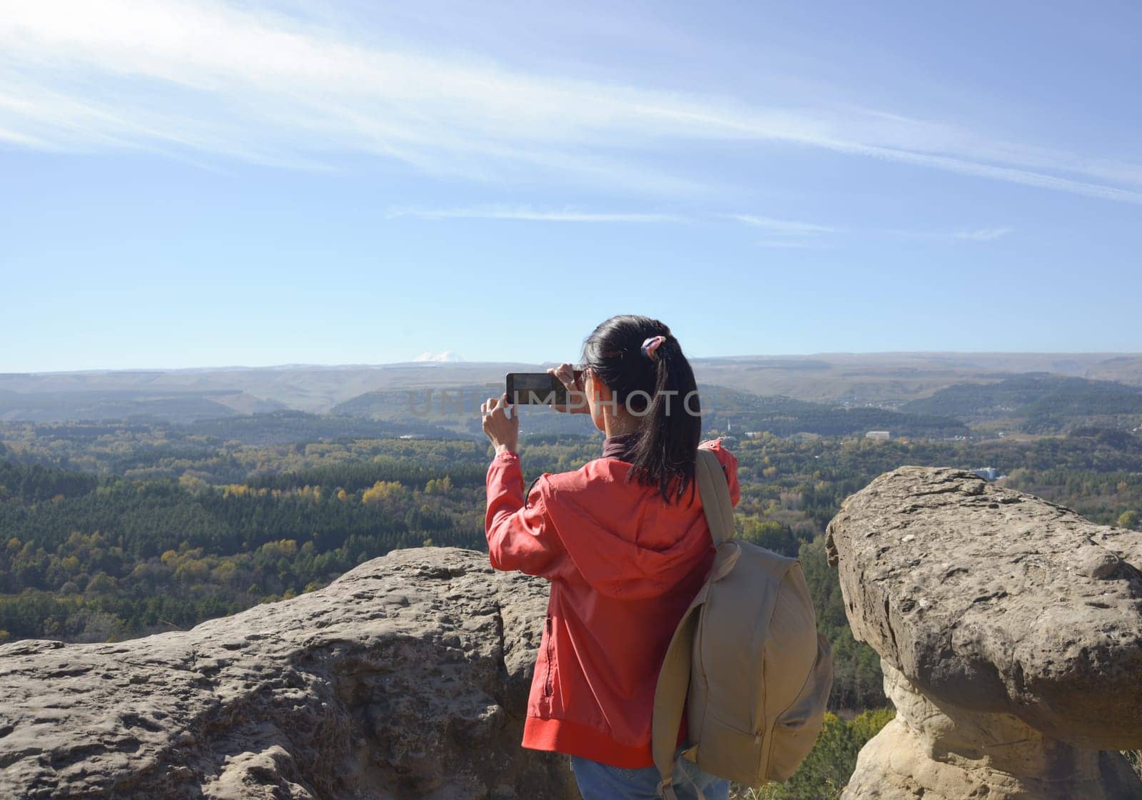 Young female traveler taking a photo of the landscape on a sunny day at the top of the mountain. Hiking and rock climbing by Ekaterina34