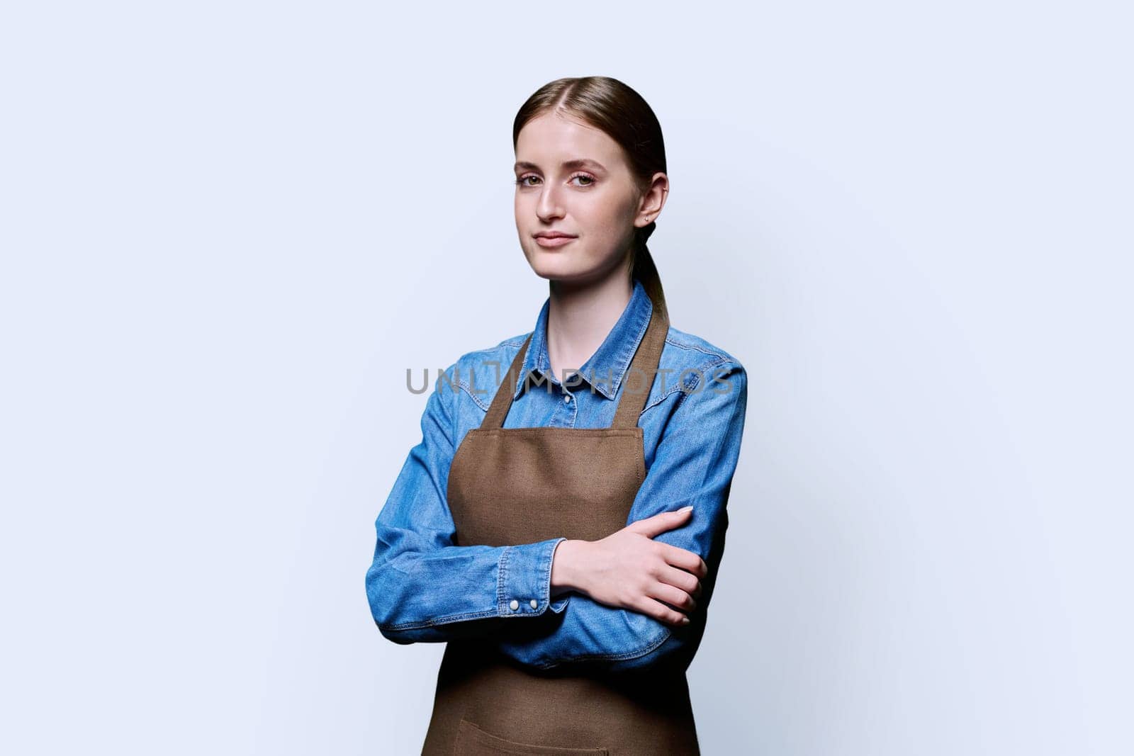 Portrait of young smiling confident woman in apron on white studio background. Successful positive female with crossed arms. Worker, startup, small business, service sector, staff, youth concept