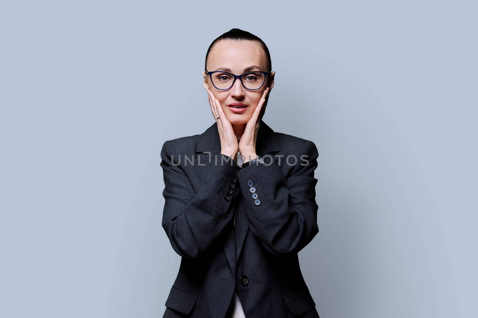 Shocked surprised businesswoman holding face with hands looking at camera on gray studio background